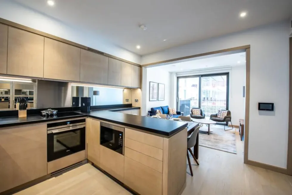 Open-plan kitchen in pale wood with black worktops and a breakfast bar, looking through to the reception room