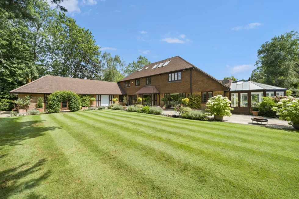 Rear elevation and striped lawn at Silver Birch, with conservatory, paved terrace and hydrangea borders