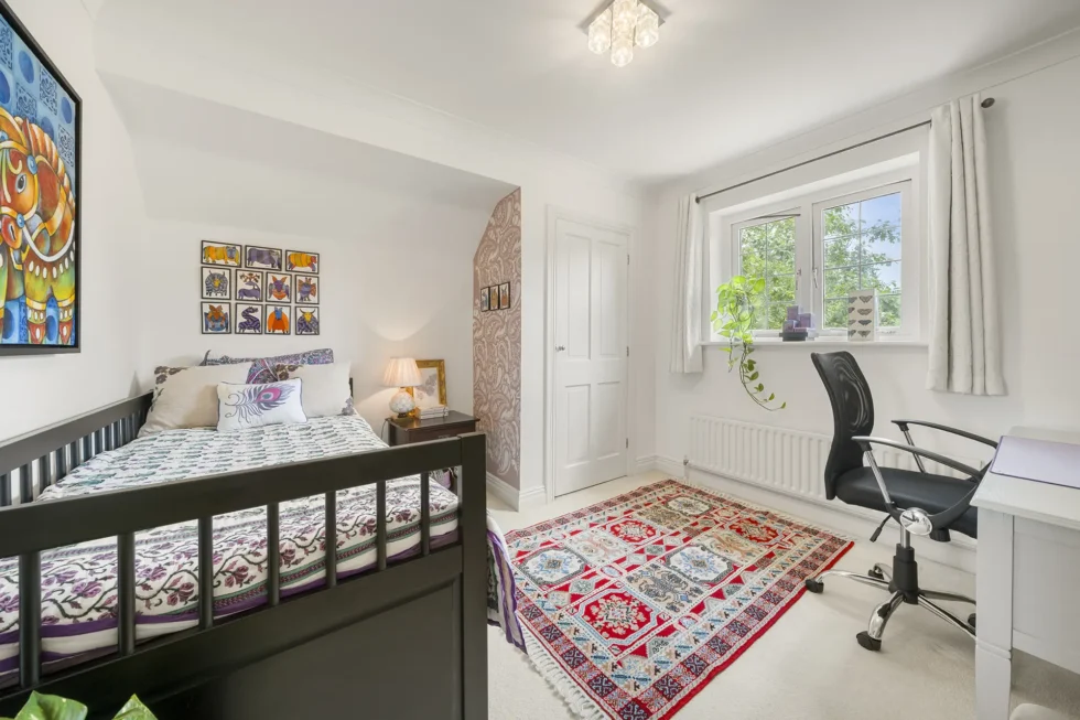 Single bedroom with raised bed, desk and study chair beside a papered alcove