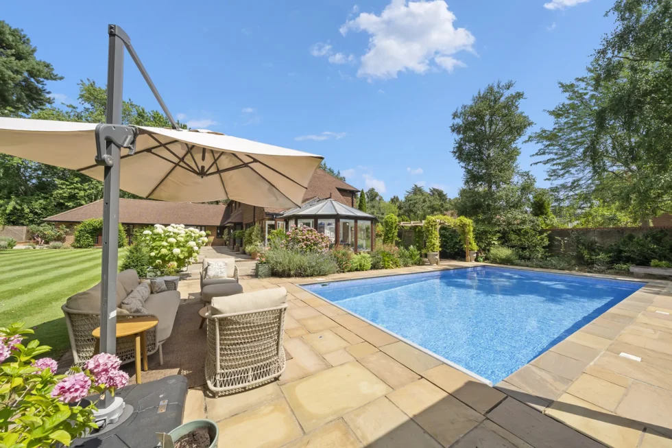 Swimming pool and terrace seating under a cantilever parasol, looking back towards the conservatory