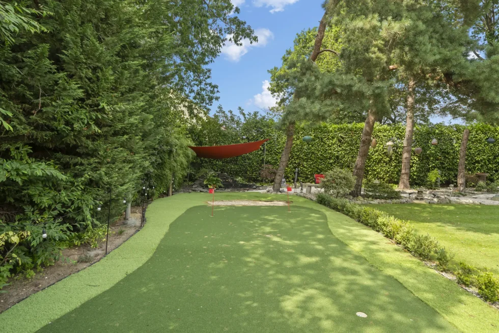 Golf putting green with two flags, set within the garden beneath mature pines