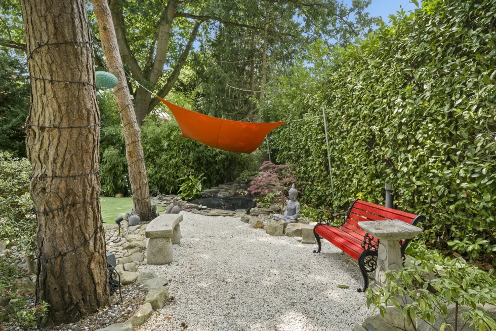 Gravel seating area beside a rock water feature, with stone benches, statuary and shade sail